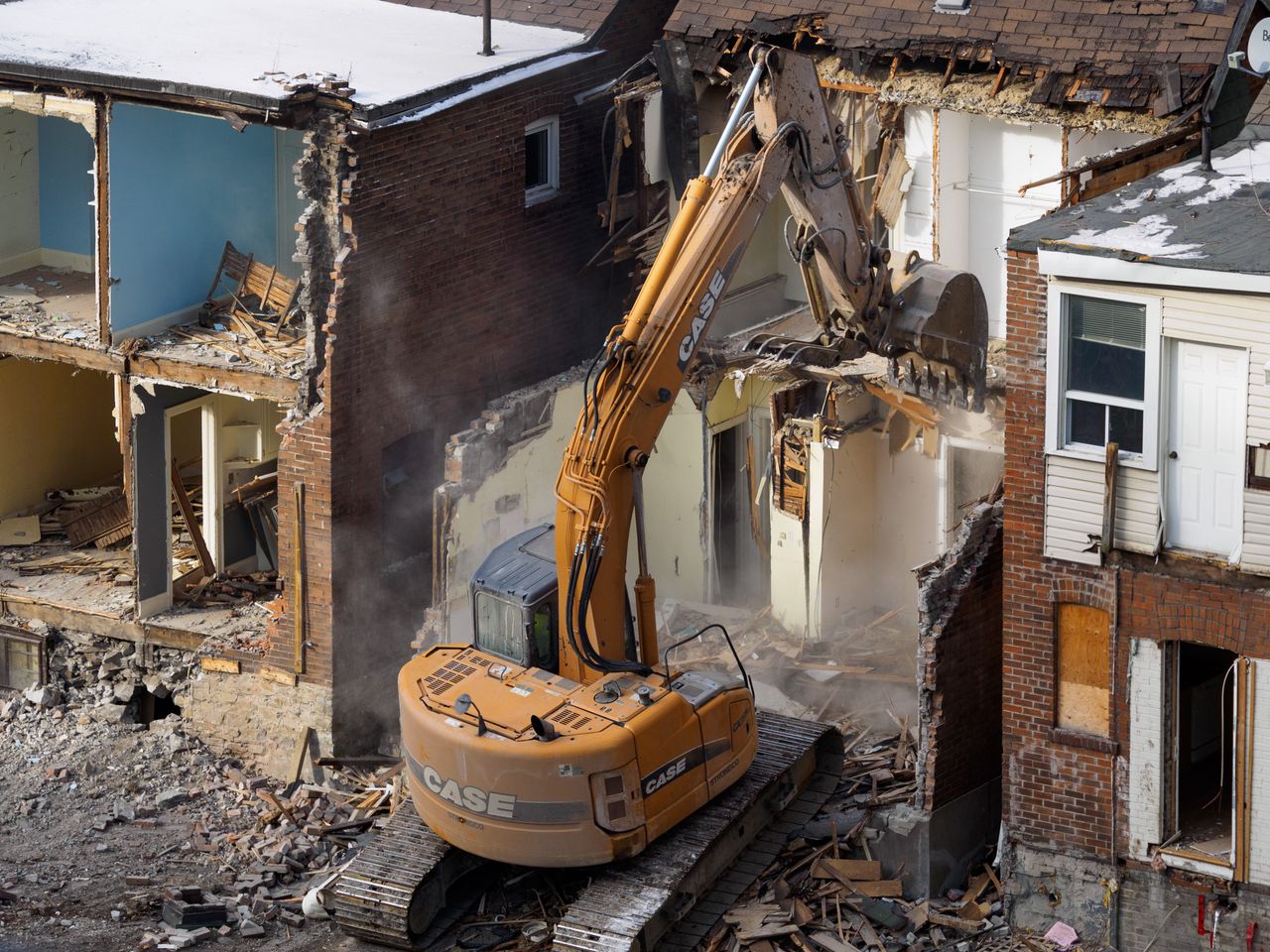 Yellow CASE demolition excavator tearing into a brick building with debris and dust around the site